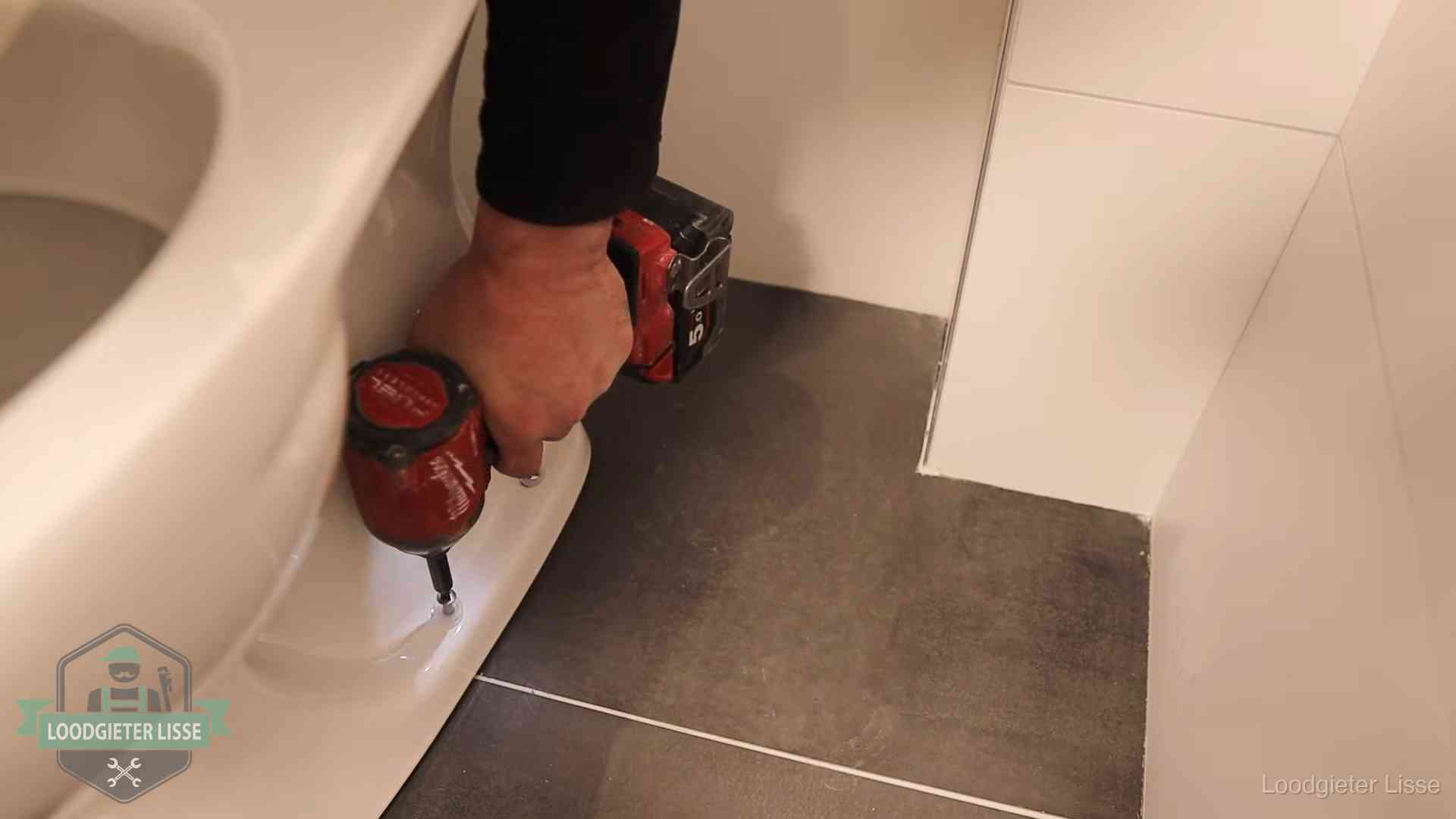 Loodgieter zet de voet van een wc-pot vast op de tegelvloer in Lisse